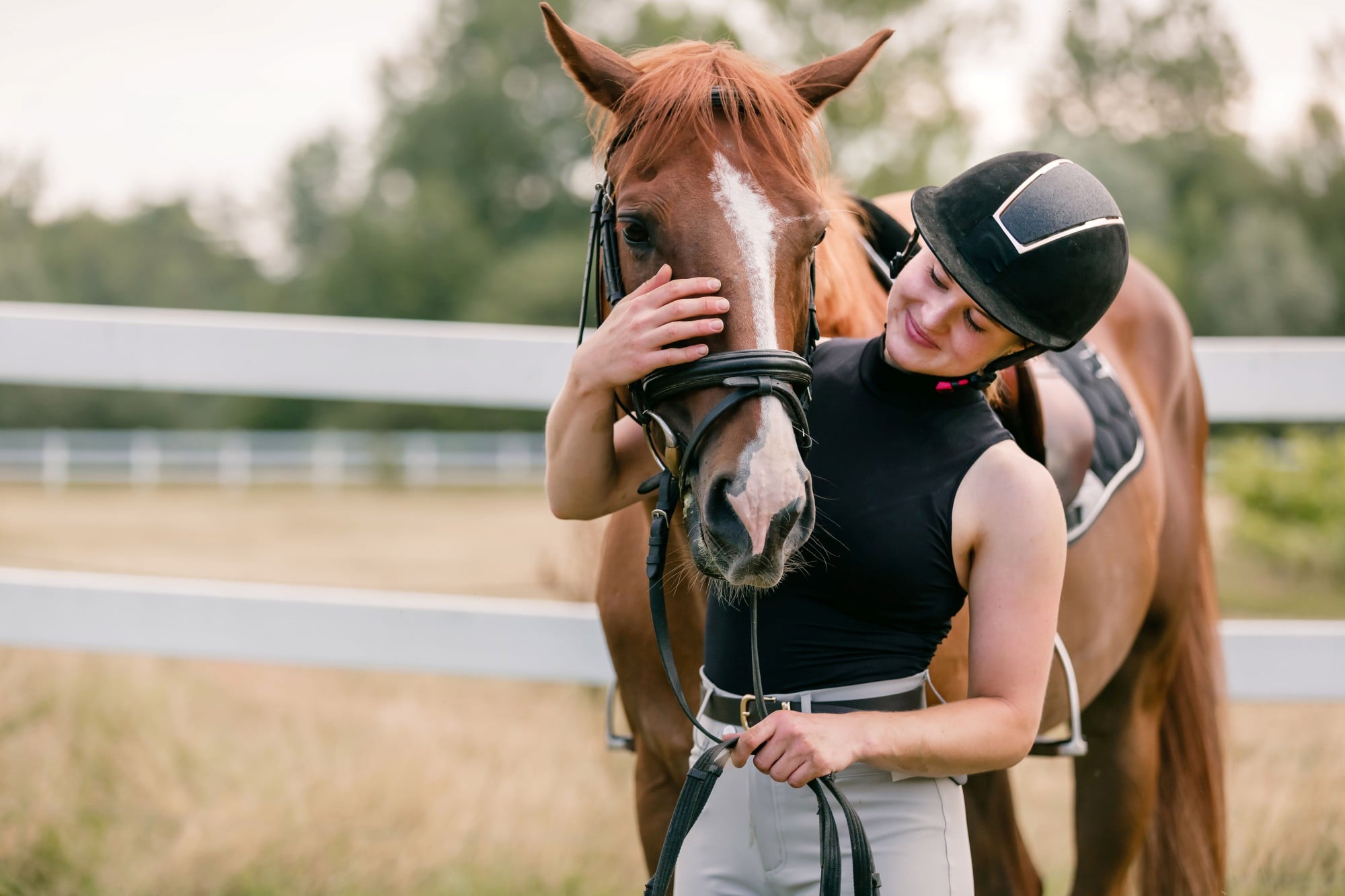 woman in riding gear hugs her brown horse