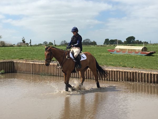 Charlotte riding Oggie through the water on a cross country course